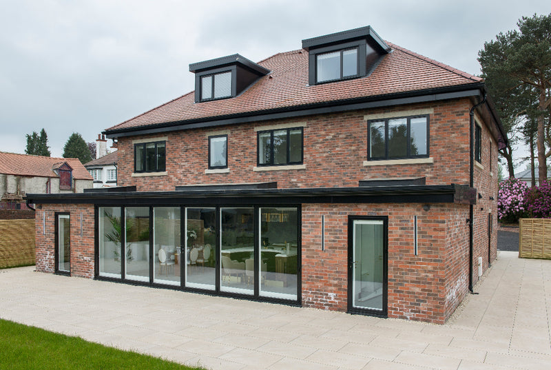 Modern brick house with large glass windows and a red roof.
