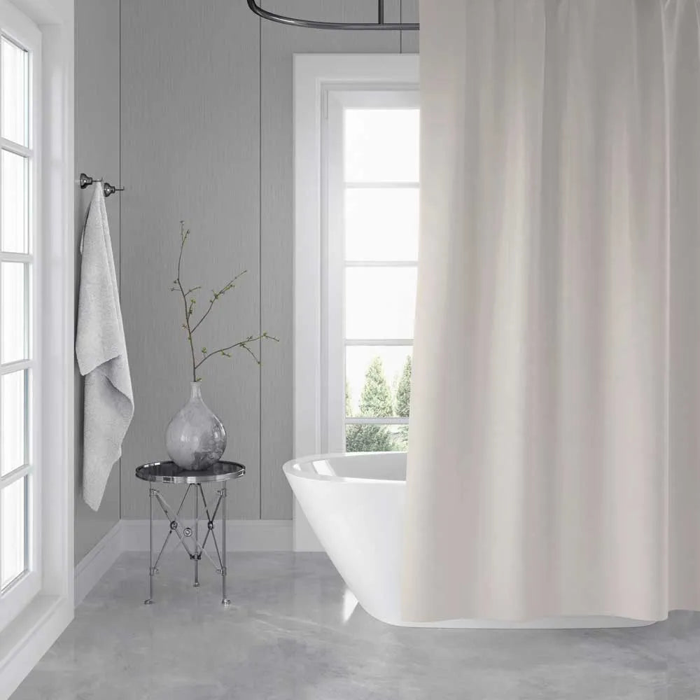 A white fabric shower curtain hanging in a bright, modern bathroom with gray paneled walls, a freestanding white tub, and a small side table with a vase.