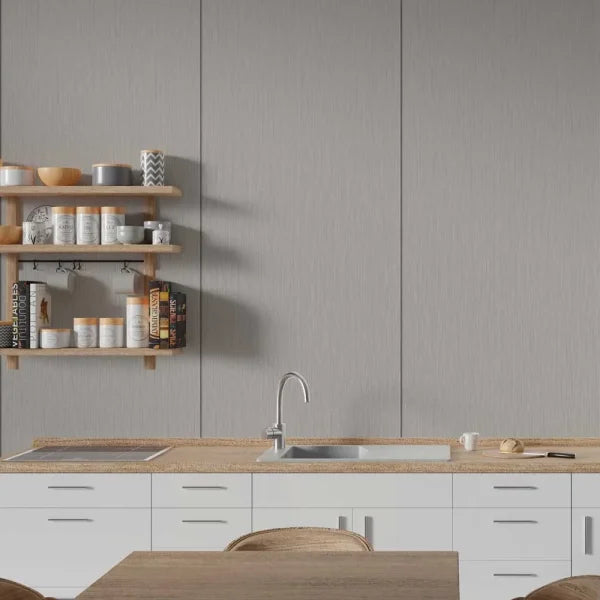 A modern kitchen interior with a large textured gray wall panel behind a white countertop, integrated sink, and light wood shelving with cookware and books.