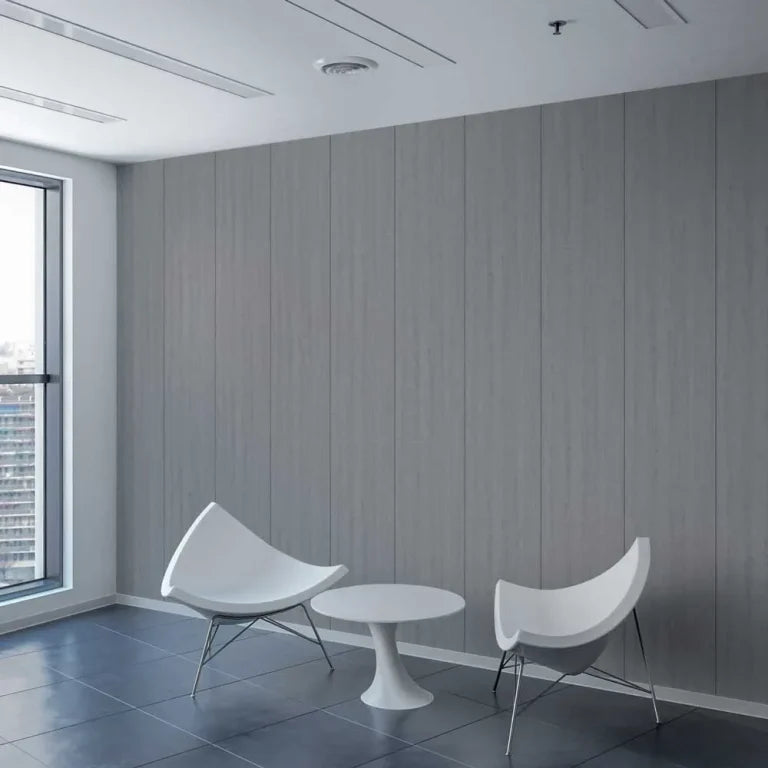 A modern interior scene with two white curved chairs and a small round white table set against a gray wood-paneled wall, with a large window on the left showing a city view.