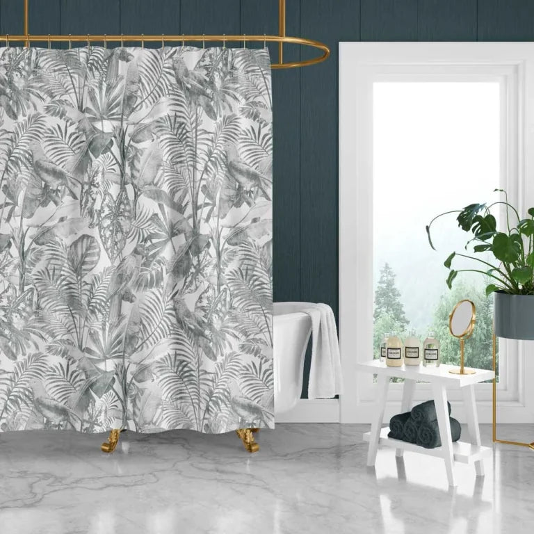 A tropical palm leaf shower curtain in a gray and white botanical pattern hanging in a modern bathroom with a white tub, marble floor, and dark teal wood-paneled walls.