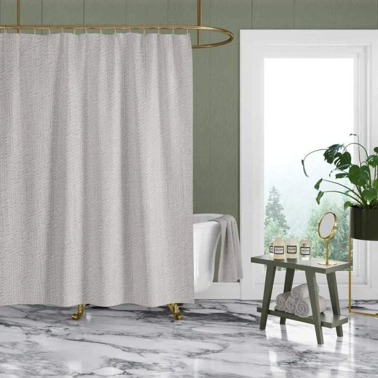 A textured light gray shower curtain hanging in a modern bathroom with a white tub, marble floor, green walls, and a gold shower rod.