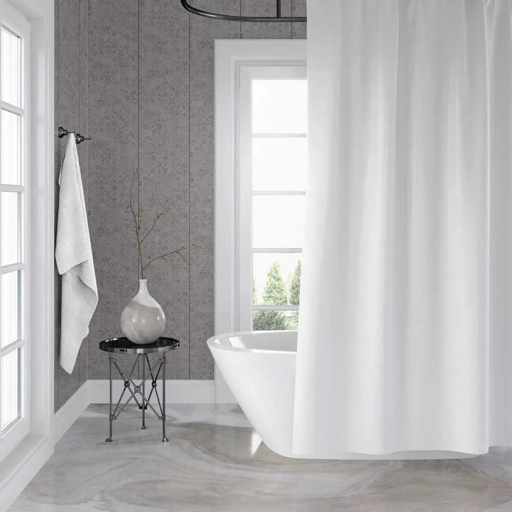 A white fabric shower curtain hanging in a bright, modern bathroom with gray textured walls, a freestanding white tub, and a small side table with a vase.