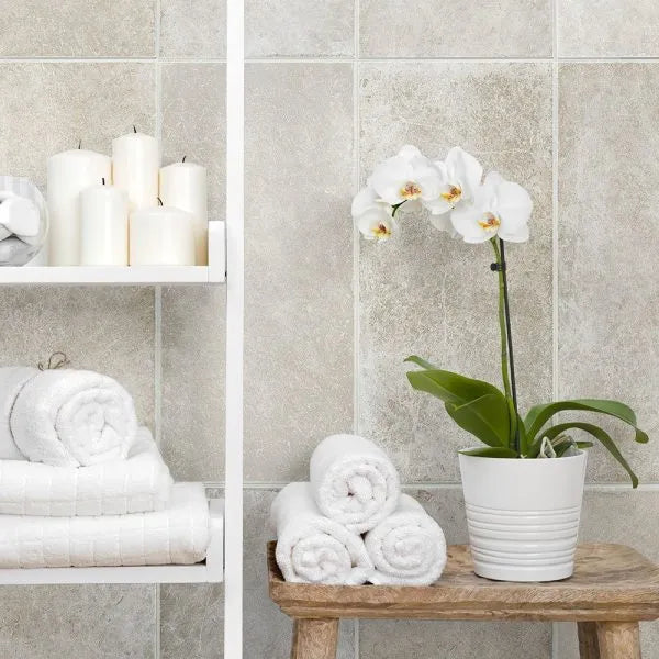 Bathroom setting with white towels, candles, and a potted orchid on a wooden stool.