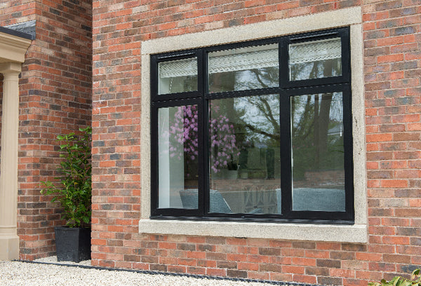 Window with black aluminium frame on a brick wall, reflecting trees and a building.