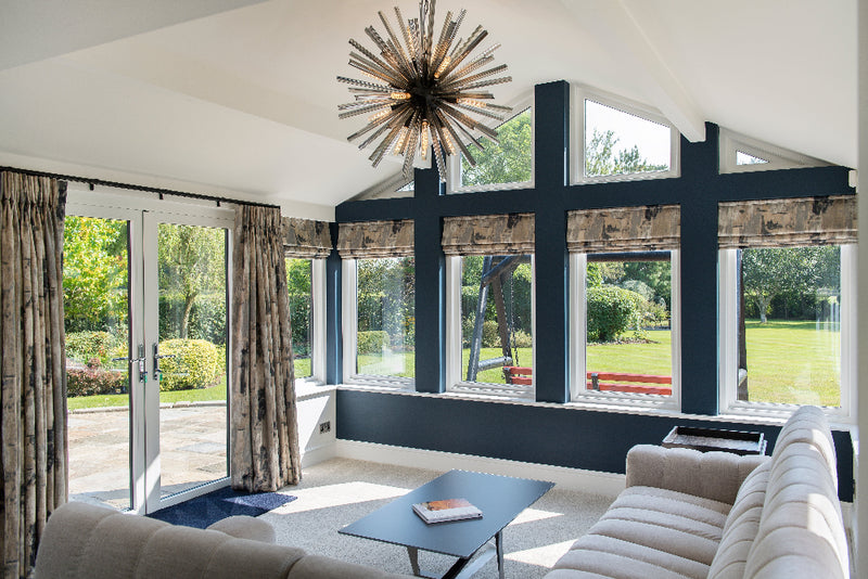 Modern living room with large windows, beige sofa, and decorative chandelier.