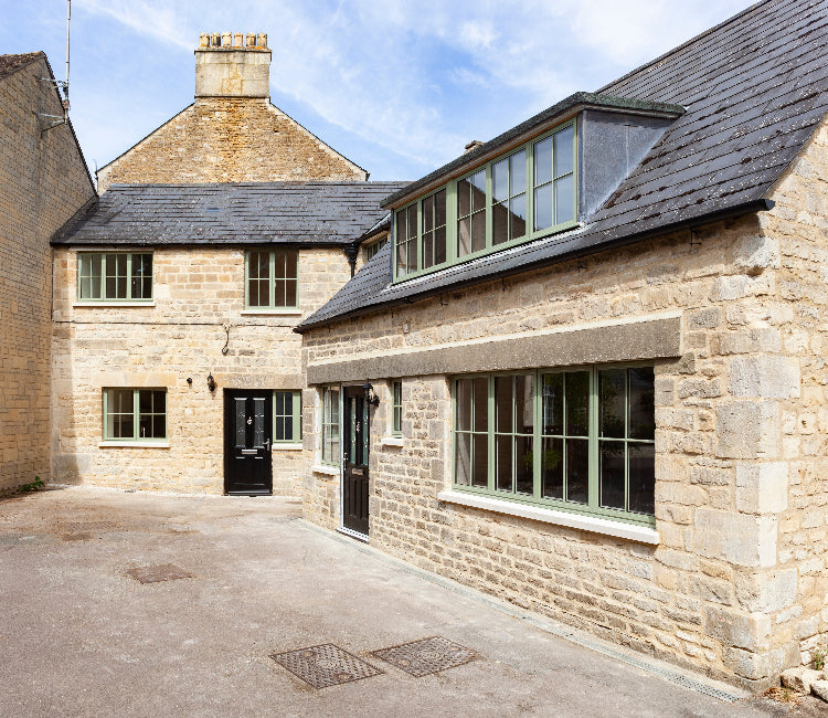 Stone house with modern green windows and extension under a blue sky