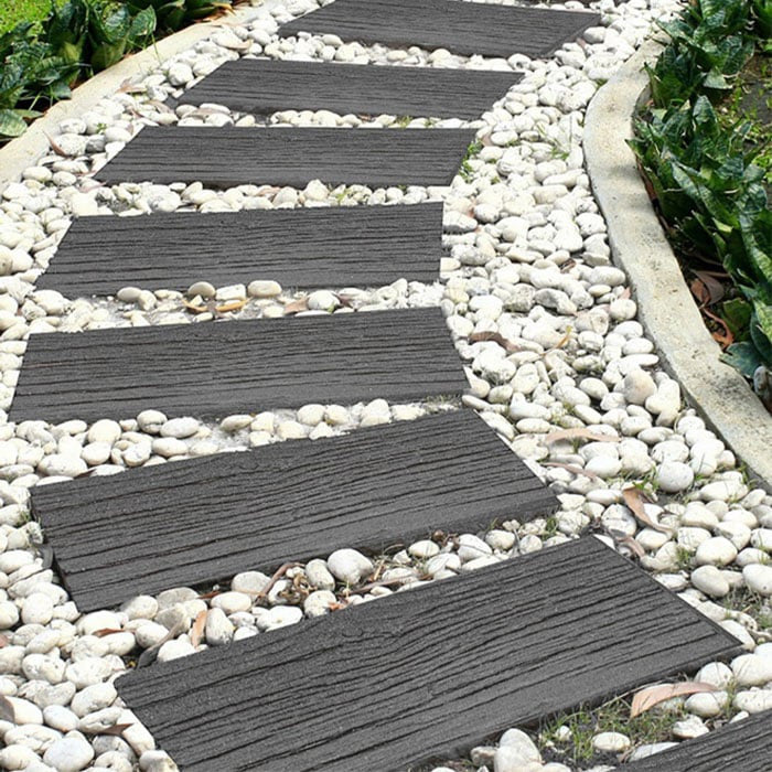 Dark gray rectangular stepping stones with a wood-grain texture, arranged in a curved garden path over white pebbles.