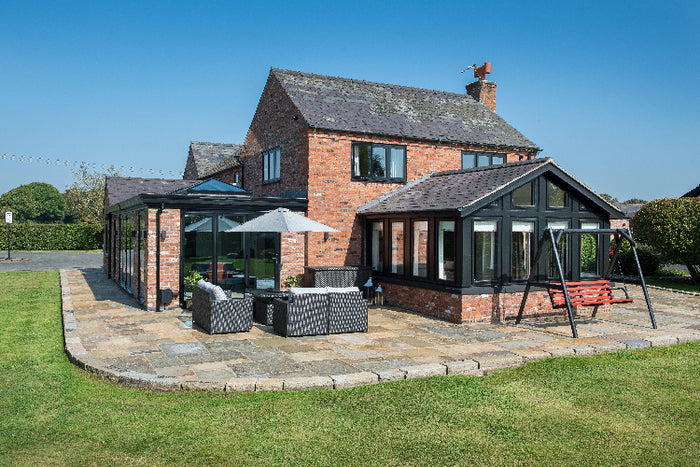 Brick house with a modern extension and outdoor seating area on a sunny day.