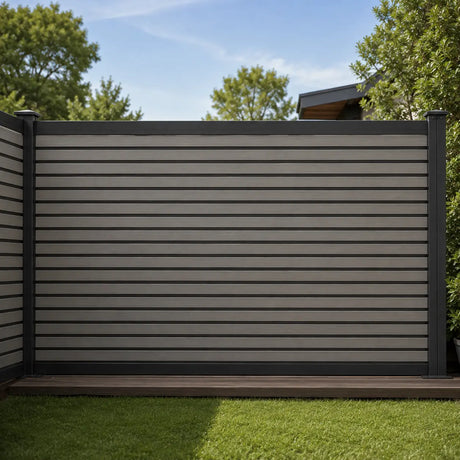 A modern horizontal slat fence installed in a backyard, featuring light gray panels with dark gray posts and trim, set against a background of green trees and blue sky.
