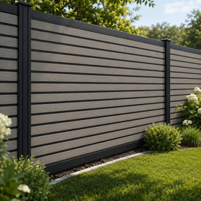 A modern horizontal slat vinyl fence with dark gray panels and black posts installed in a landscaped yard with green grass and shrubs.