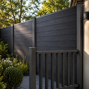 Dark charcoal composite fencing with a matching gate and railing, installed on a backyard patio with green shrubs and trees in the background.