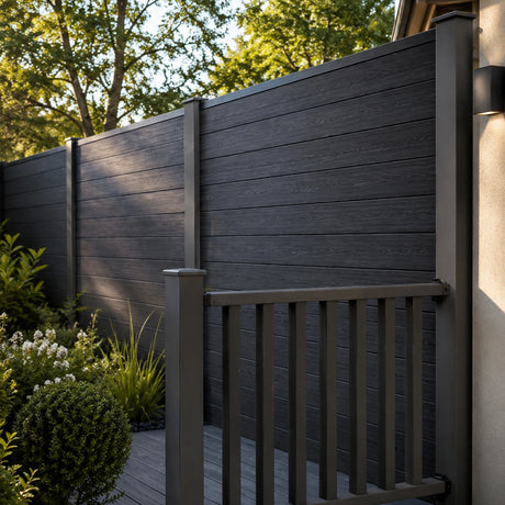Dark charcoal composite fencing with a matching gate and railing, installed on a backyard patio with green shrubs and trees in the background.