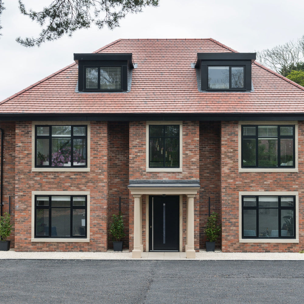 Two-story brick house with black windows and a red roof.