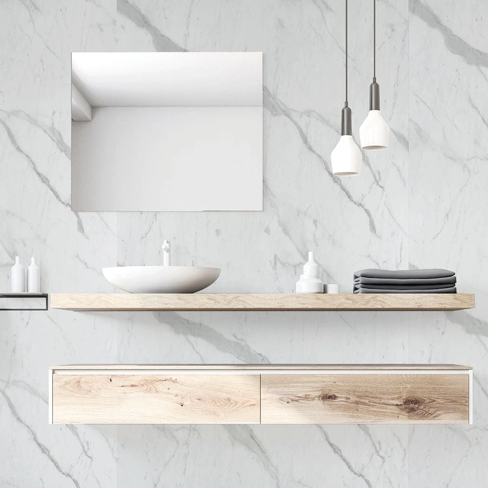 A modern floating bathroom vanity setup with a light wood shelf and matching cabinet against a white marble wall, featuring a white vessel sink, a rectangular mirror, two pendant lights, and folded towels.