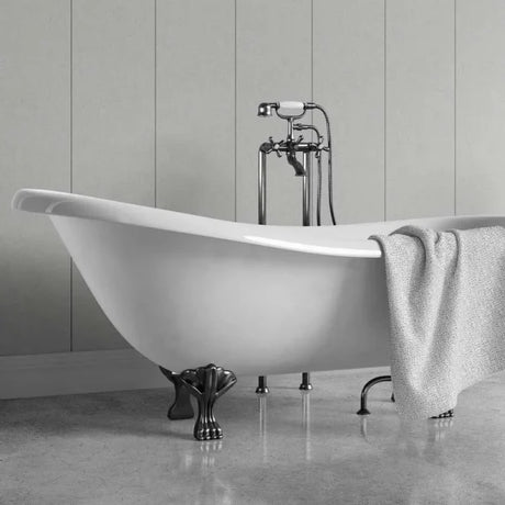 A white freestanding clawfoot bathtub with dark metal legs and a matching wall-mounted faucet, shown in a bathroom setting with a gray towel draped over the side.