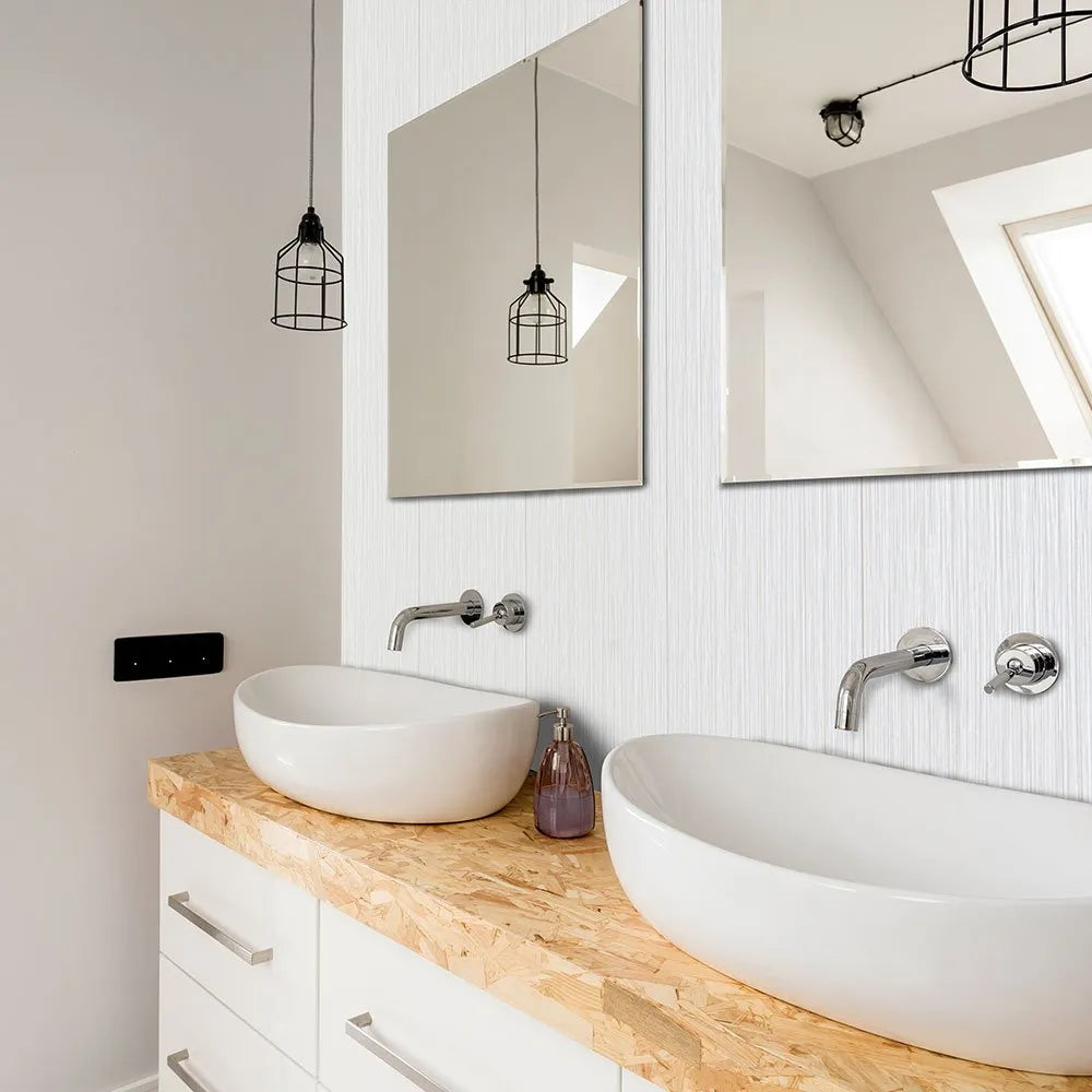 Modern double bathroom vanity with two white oval vessel sinks, chrome faucets, a light wood countertop, white cabinets, and large wall mirrors above. Pendant lights hang from the ceiling, and a window with skylight is reflected in the mirrors.