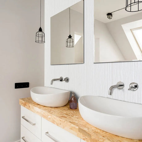 Modern double bathroom vanity with two white oval vessel sinks, chrome faucets, a light wood countertop, white cabinets, and large wall mirrors above. Pendant lights hang from the ceiling, and a window with skylight is reflected in the mirrors.