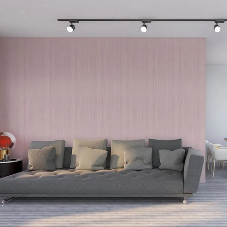 A modern gray tufted sofa with multiple gray and beige throw pillows, set against a light pink paneled wall in a contemporary living room.