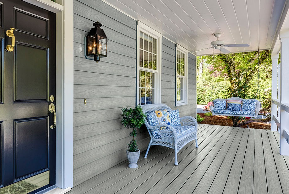 Front porch of a house with a dark door, light gray siding, and outdoor furniture.
