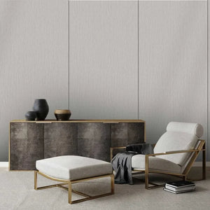 A modern living room setup featuring a light beige upholstered armchair with a gold metal frame, a matching ottoman, a low sideboard with textured dark gray panels and gold trim, and decorative ceramic vases on top.