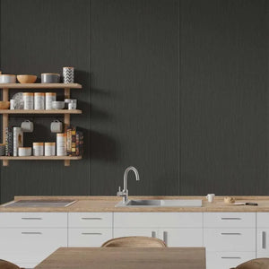 A modern kitchen scene with a large dark charcoal textured wall panel behind a light wood countertop, white cabinets, a sink, and floating wooden shelves holding dishes and mugs.