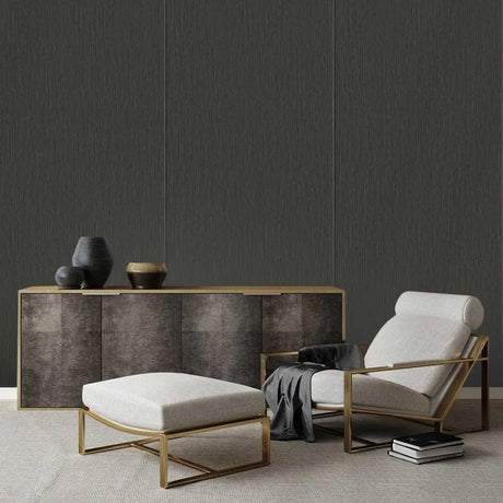 A modern lounge room scene featuring a light beige upholstered armchair with a gold metal frame, a matching ottoman, a textured wood sideboard, and a dark charcoal wall.