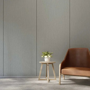A modern interior scene with a brown leather armchair, a small light wood side table holding a potted plant, and a textured gray wall behind them.
