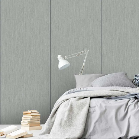 A styled bedroom scene featuring a bed with light gray bedding, a white adjustable desk lamp, and a stack of books on a bedside table against a textured gray paneled wall.