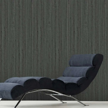A modern chaise lounge chair upholstered in dark blue-gray fabric with a curved chrome metal base, set against a dark gray wood-paneled wall.