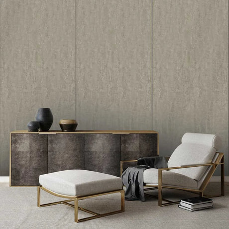 A modern living room setup featuring a light beige upholstered armchair with a gold metal frame, a matching beige ottoman with a gold frame, and a dark wood sideboard against a textured beige paneled wall.