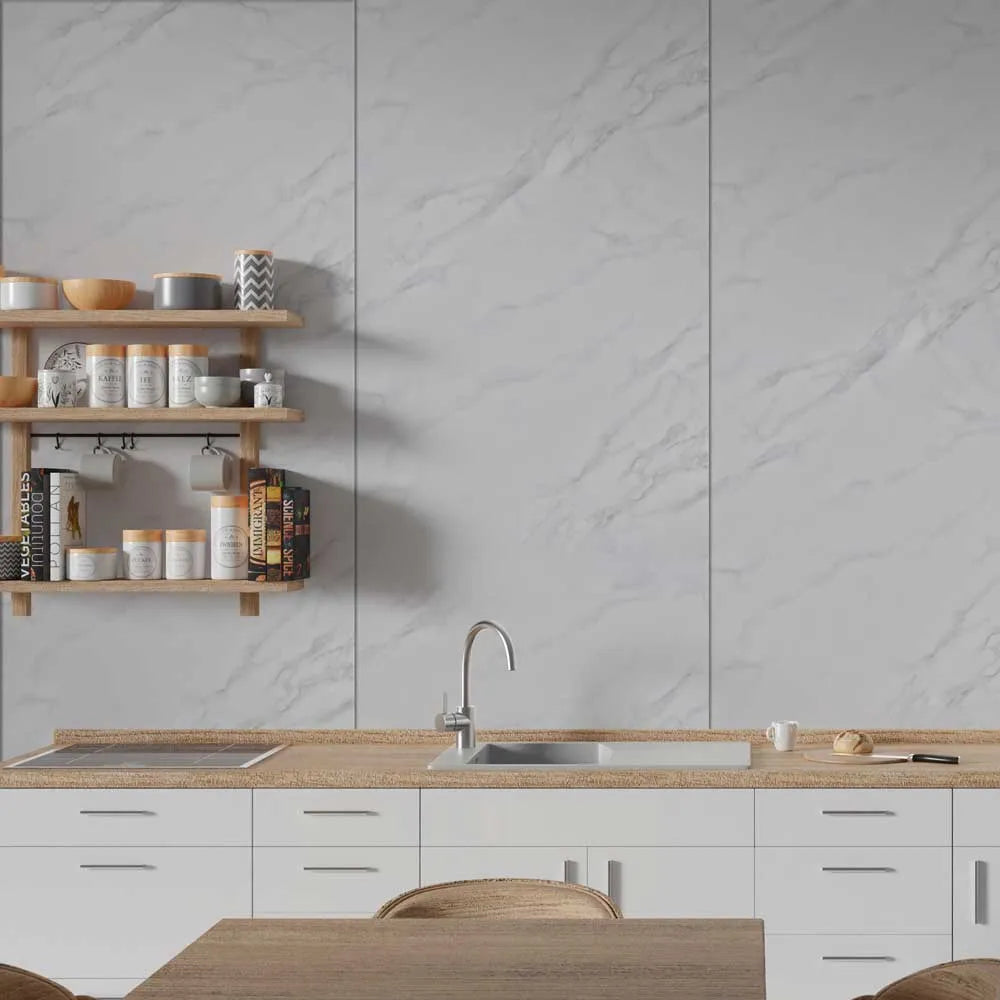 A modern kitchen interior with white marble-look wall panels, a light wood countertop, white cabinets, a built-in sink, and floating wooden shelves holding jars and cookware.