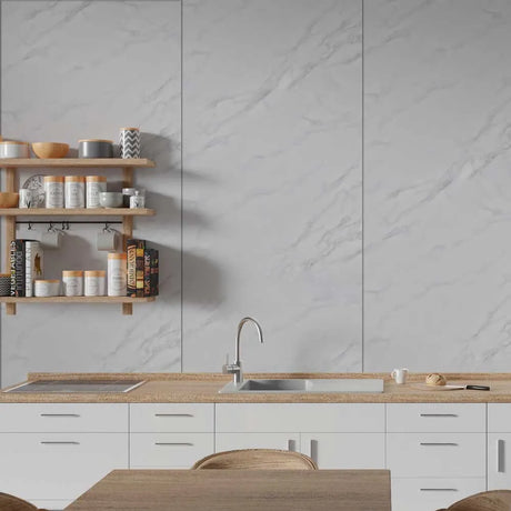 A modern kitchen interior with white marble-look wall panels, a light wood countertop, white cabinets, a built-in sink, and floating wooden shelves holding jars and cookware.