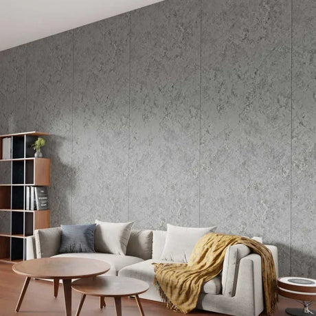 A modern living room featuring a large wall made of textured gray stone or concrete-look panels behind a light gray sofa with pillows and a mustard throw blanket.