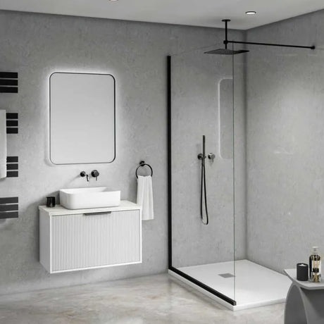 Modern bathroom interior with a white vessel sink, white wall-mounted vanity, rectangular mirror with backlighting, black shower glass enclosure, and gray textured walls and floor.