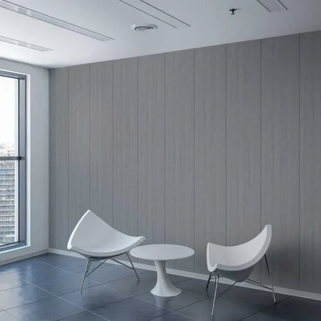 A modern interior scene with two white curved chairs and a small round white table set against a gray wood-paneled wall, with a large window on the left showing a city view.