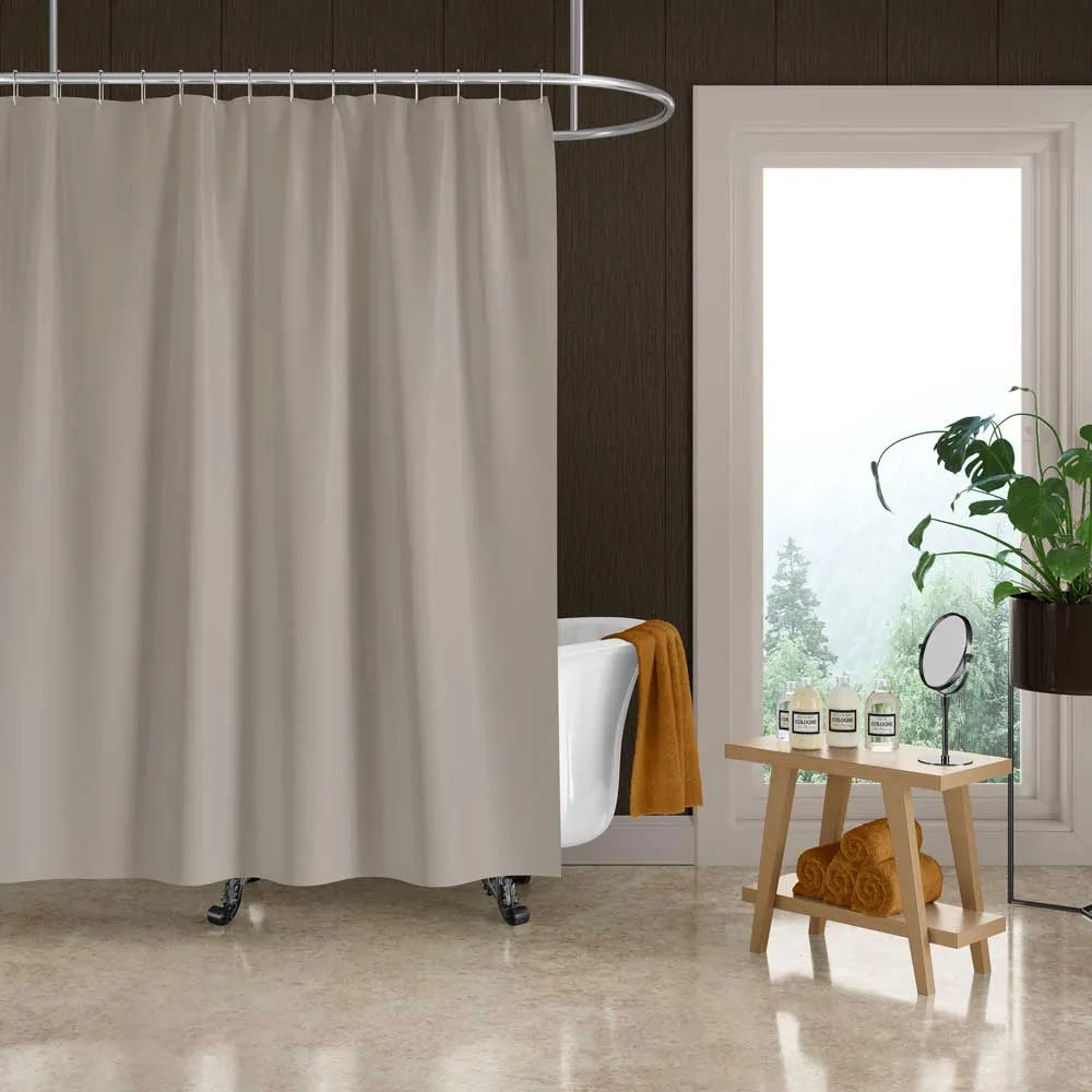 A light beige fabric shower curtain hanging in a bathroom setting with a white clawfoot tub, a small wooden side table, and a window.