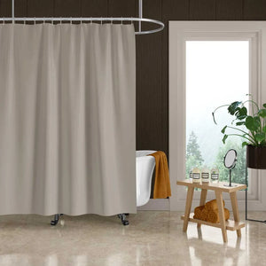 A light beige fabric shower curtain hanging in a bathroom setting with a white clawfoot tub, a small wooden side table, and a window.