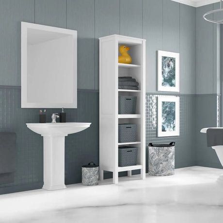 A tall white bathroom storage cabinet with five open shelves stands next to a white pedestal sink. The cabinet has three upper open shelves, two middle shelves with gray woven baskets, and one lower shelf with a gray patterned basket.