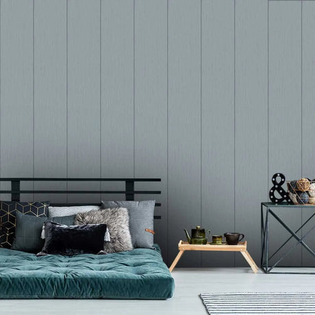 A styled bedroom interior featuring a gray wood-paneled wall, a teal tufted mattress on a black metal frame, decorative pillows, a small wooden tray table with a teapot, and a black metal side table with decor.