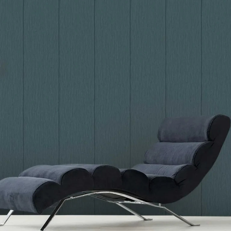 A modern lounge chair with a dark blue-gray upholstered body and curved chrome legs, set against a dark blue-gray paneled wall.