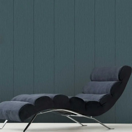 A modern lounge chair with a dark blue-gray upholstered body and curved chrome legs, set against a dark blue-gray paneled wall.
