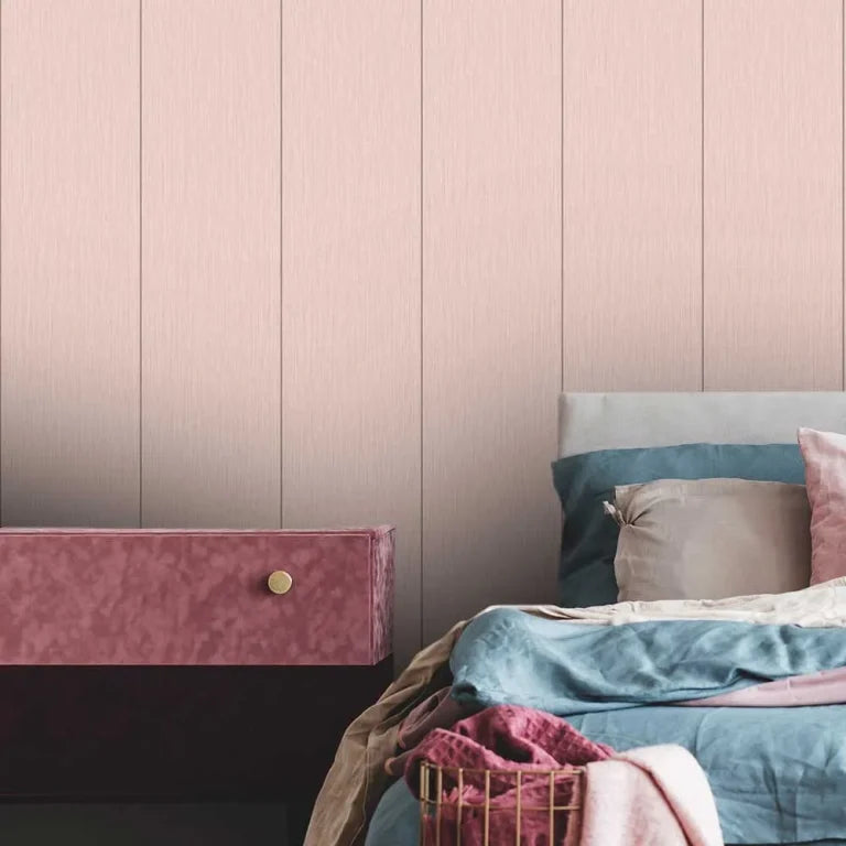 A styled bedroom corner featuring a dusty pink textured wall with vertical panel lines, a matching pink velvet floating nightstand with a gold knob, and a bed with blue and pink bedding.