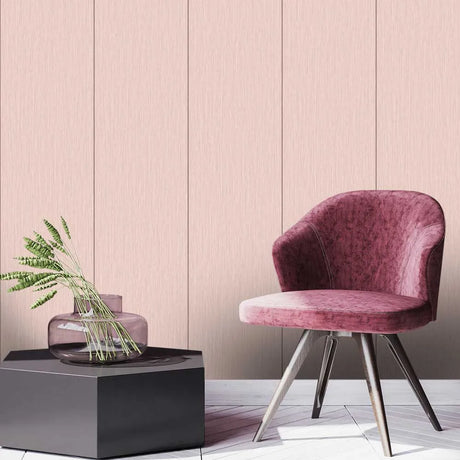 A modern interior scene with a pink upholstered accent chair on metal legs beside a dark pedestal holding a glass vase with green stems. The background is a pale blush wall with vertical panel lines.