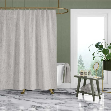 A textured light gray shower curtain hanging in a modern bathroom with a white tub, marble floor, green walls, and a gold shower rod.