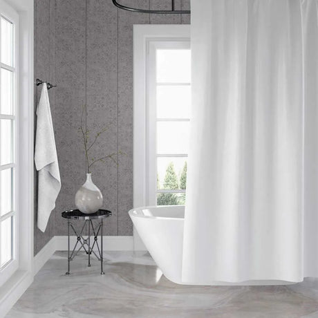 A white fabric shower curtain hanging in a bright, modern bathroom with gray textured walls, a freestanding white tub, and a small side table with a vase.