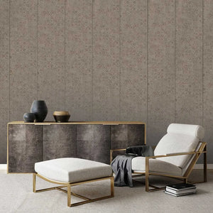 A styled interior scene showing a beige upholstered armchair with a gold metal frame, a matching ottoman, a dark wood sideboard with gold trim, and decorative vases against a patterned wallpaper background.