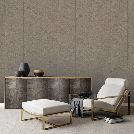 A styled interior scene showing a beige upholstered armchair with a gold metal frame, a matching ottoman, a dark wood sideboard with gold trim, and decorative vases against a patterned wallpaper background.