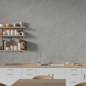 A modern kitchen scene with a large textured gray wall, white cabinets, a light wood countertop, a built-in sink, and open wooden shelves holding jars and books.