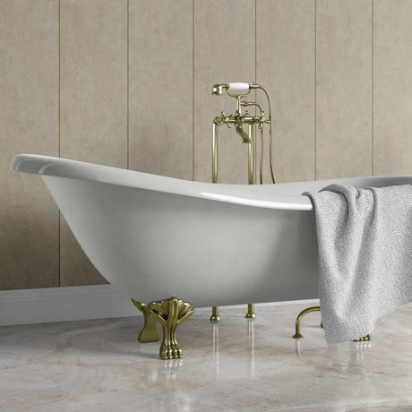 A freestanding oval bathtub with ornate gold-tone claw legs and a matching gold faucet set, shown in a bathroom with beige paneled walls and a gray towel draped over the side.
